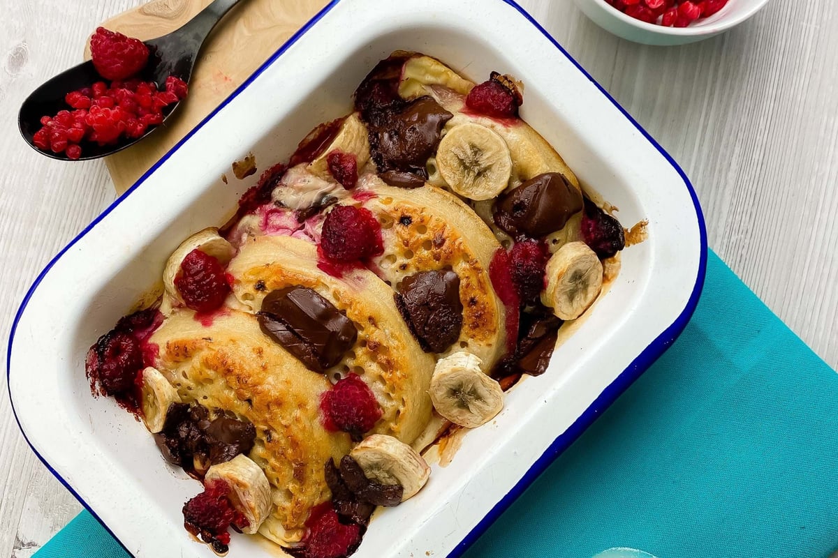 Baked pancakes with chocolate chunks, banana slices, and raspberries in a white tray.
