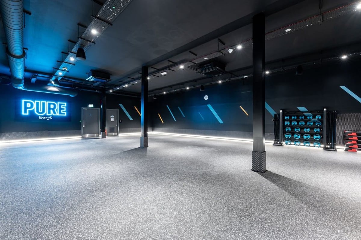 PureGym Dewsbury: Spotlights, blue-tinted interior space with electronic display board and Pure Energy branding.