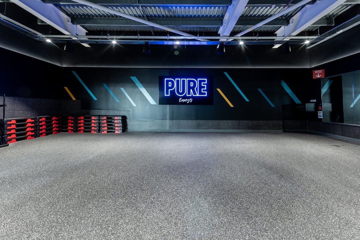 PureGym Bicester: Row of red seats, open floor space, illuminated "PURE" sign on wall.