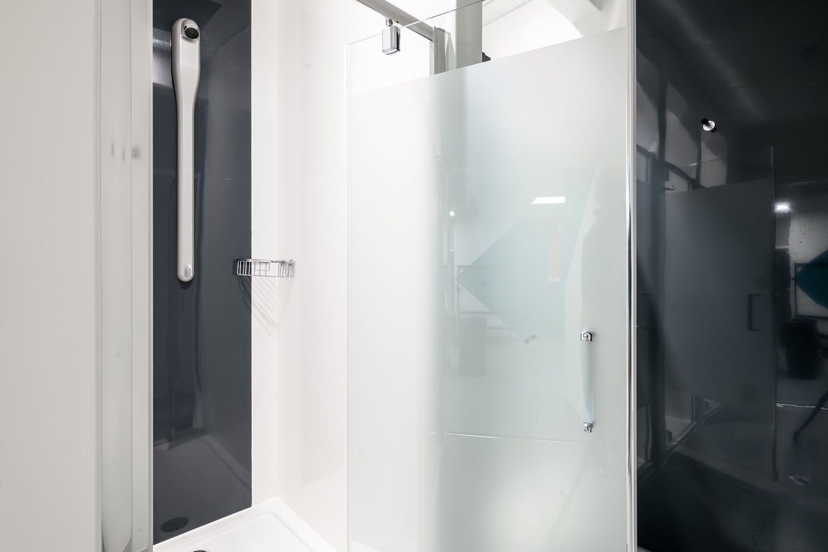 PureGym London Wimbledon: Glass shower enclosure, tiled floor and walls in a bathroom or changing room setting.