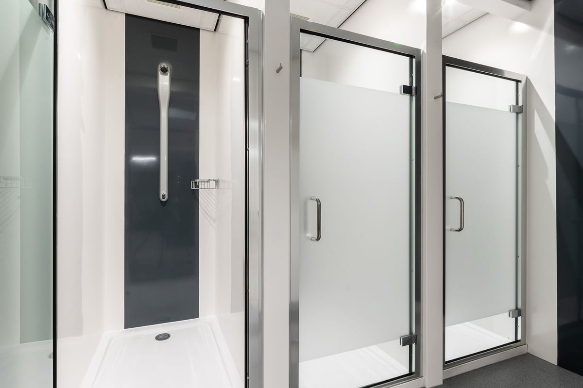 PureGym Chippenham: Shower cubicles with glass doors, benches, and tiled flooring.