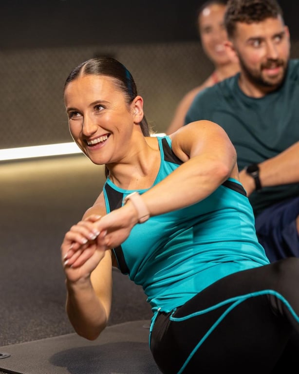 Energische Frau in türkissportlichem Oberteil lächelnd während einer Gruppenfitnesssession mit anderen in moderner Gymumgebung