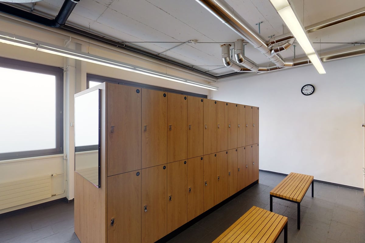 PureGym Uster: Des rangées de casiers en bois, des bancs et une horloge dans un vestiaire.