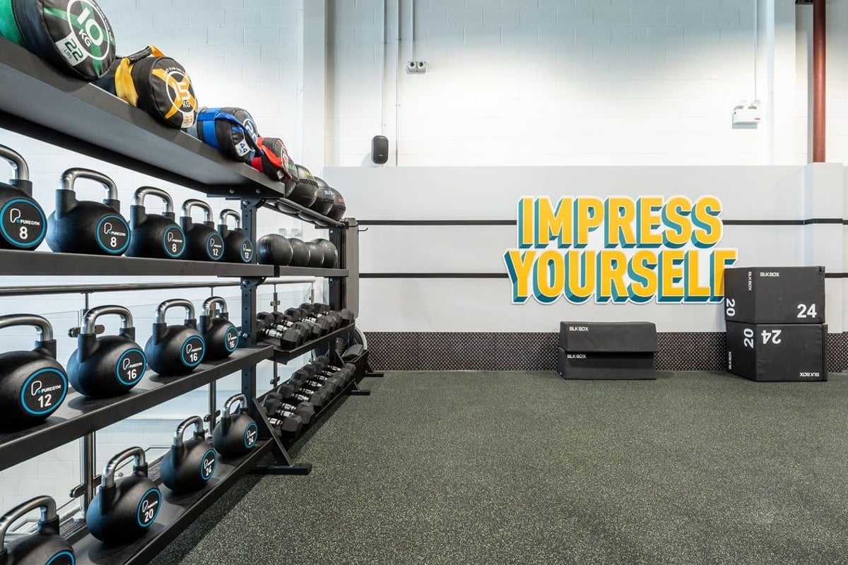 PureGym Newport Wales: Rows of kettlebells, dumbbells, weight plates, and wall graphics promoting self-improvement.
