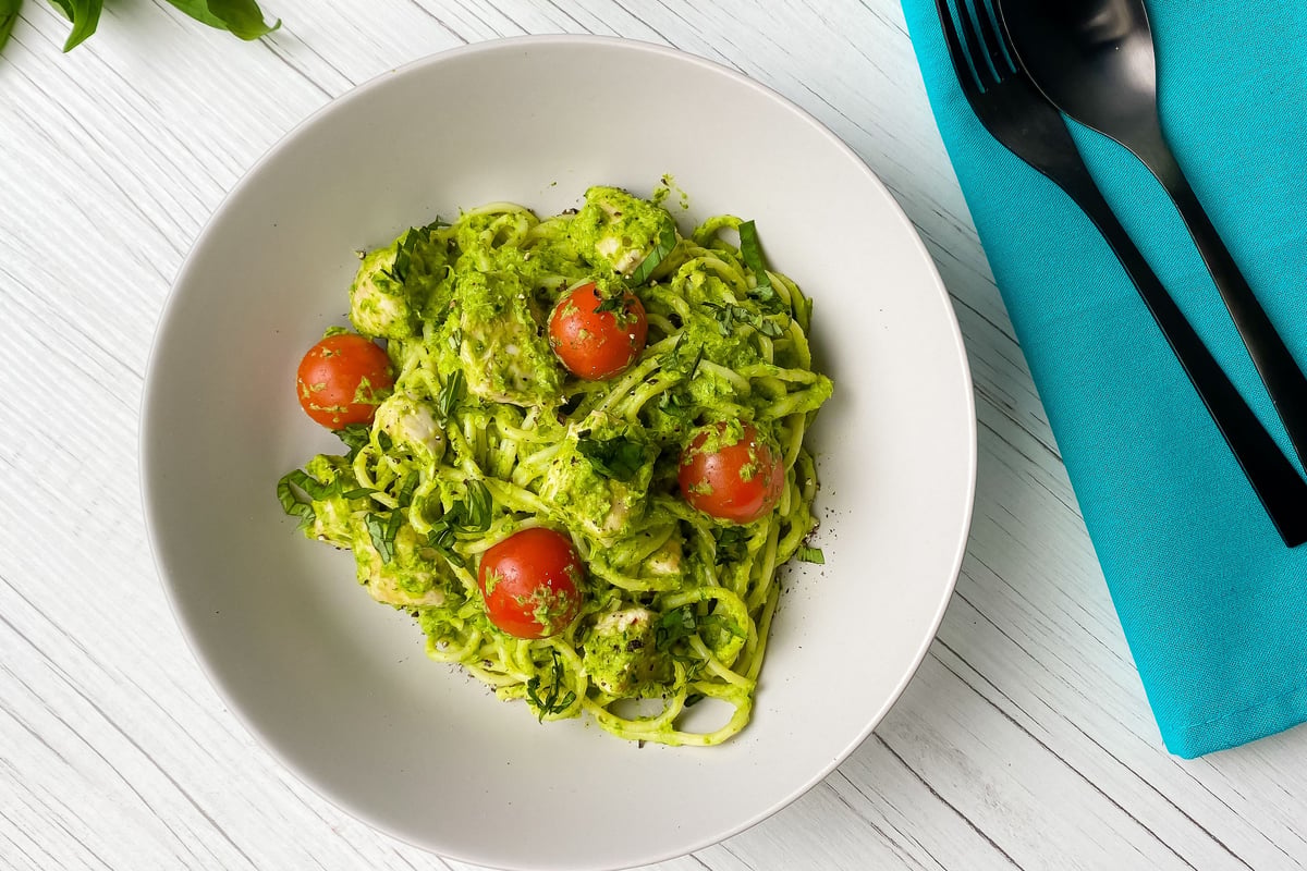 Pasta with green pesto sauce and cherry tomatoes in white bowl on wooden surface