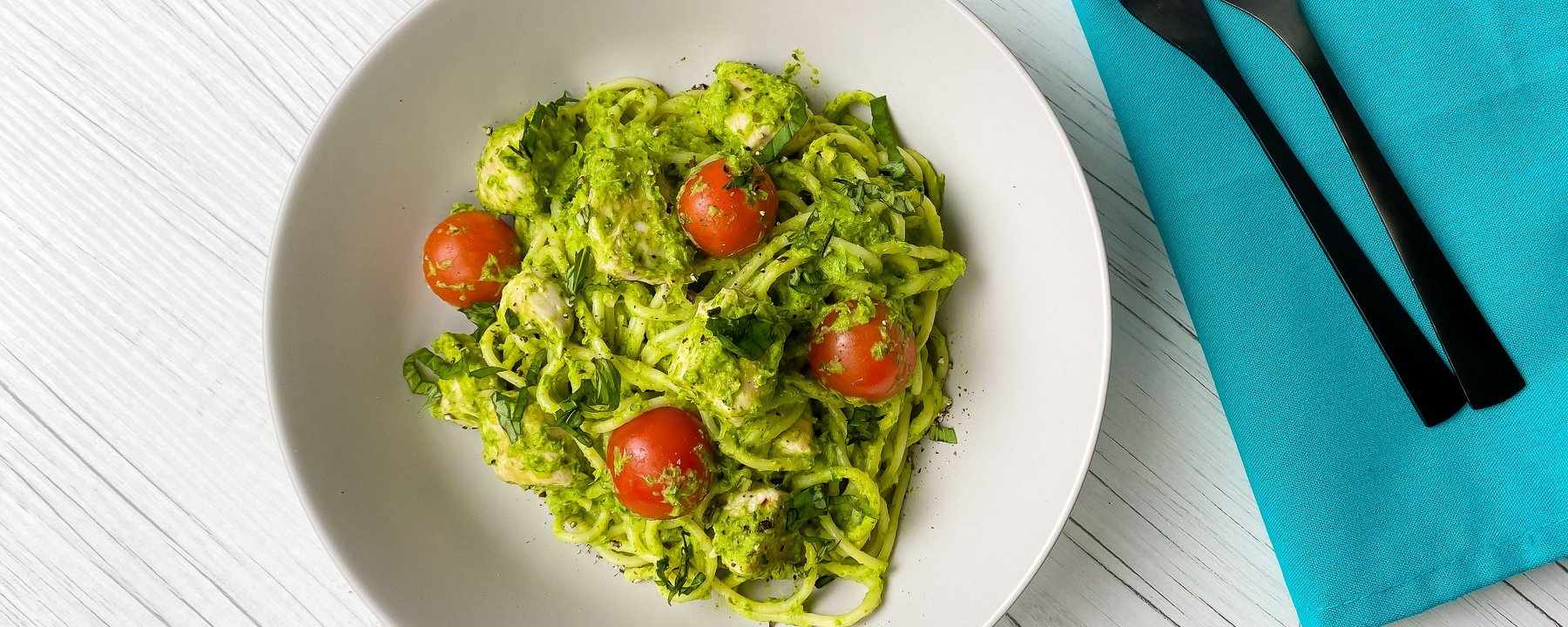 Pasta with green pesto sauce and cherry tomatoes in white bowl on wooden surface