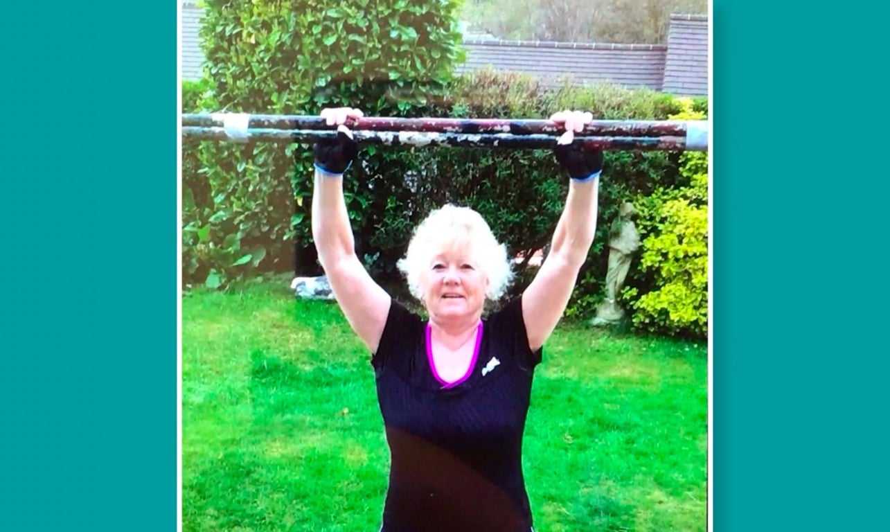Woman in black top holding a rusty metal bar above her head in a garden
