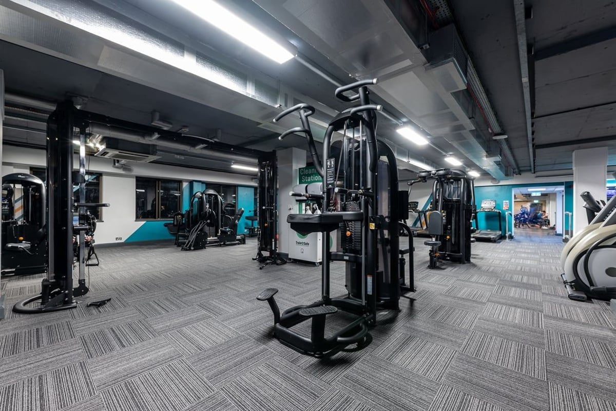 PureGym London Putney: Strength training equipment, cable machines, benches, and rubberized flooring in a dimly lit gym.