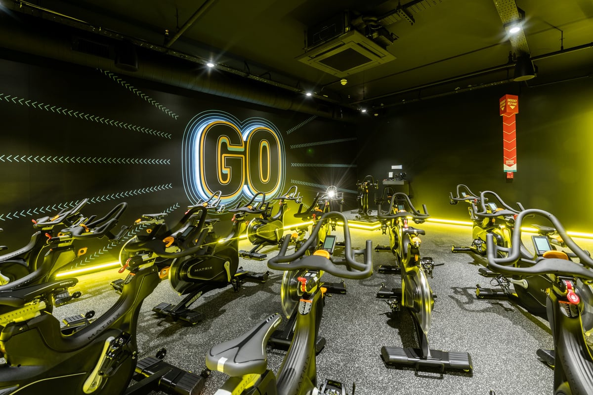 PureGym London Kingston: Row of stationary bikes inside a dimly lit studio with neon "GO" signage.