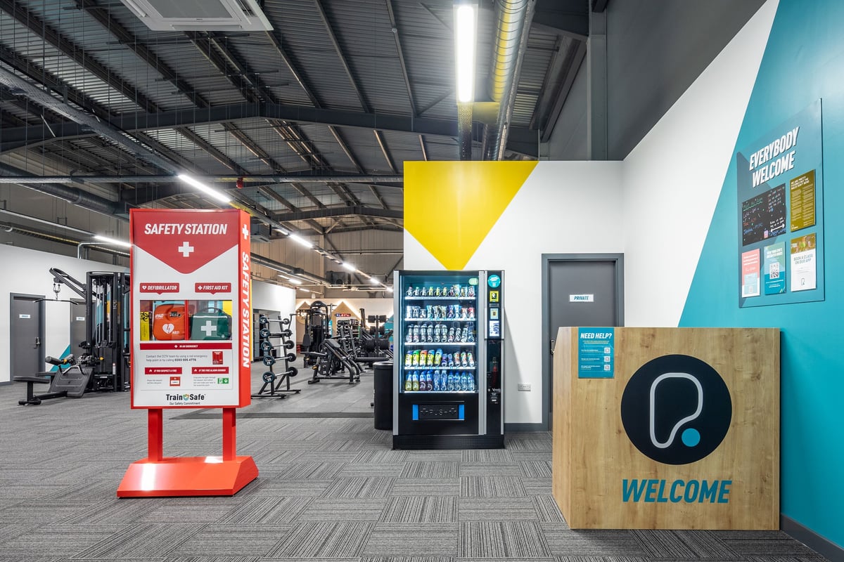 PureGym Wantage: Vending machines, safety station, welcome sign in a gym space with exercise equipment visible.