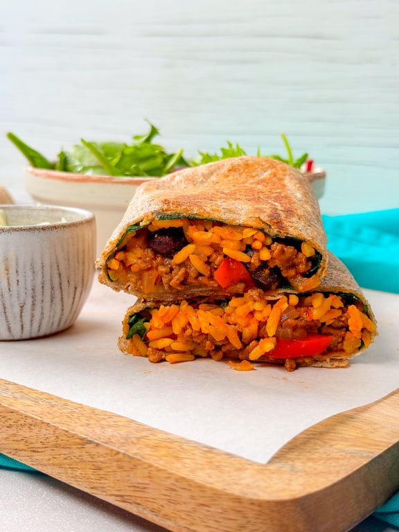 Wrap cut in half showing rice, beans, minced meat, and vegetables inside on wooden board