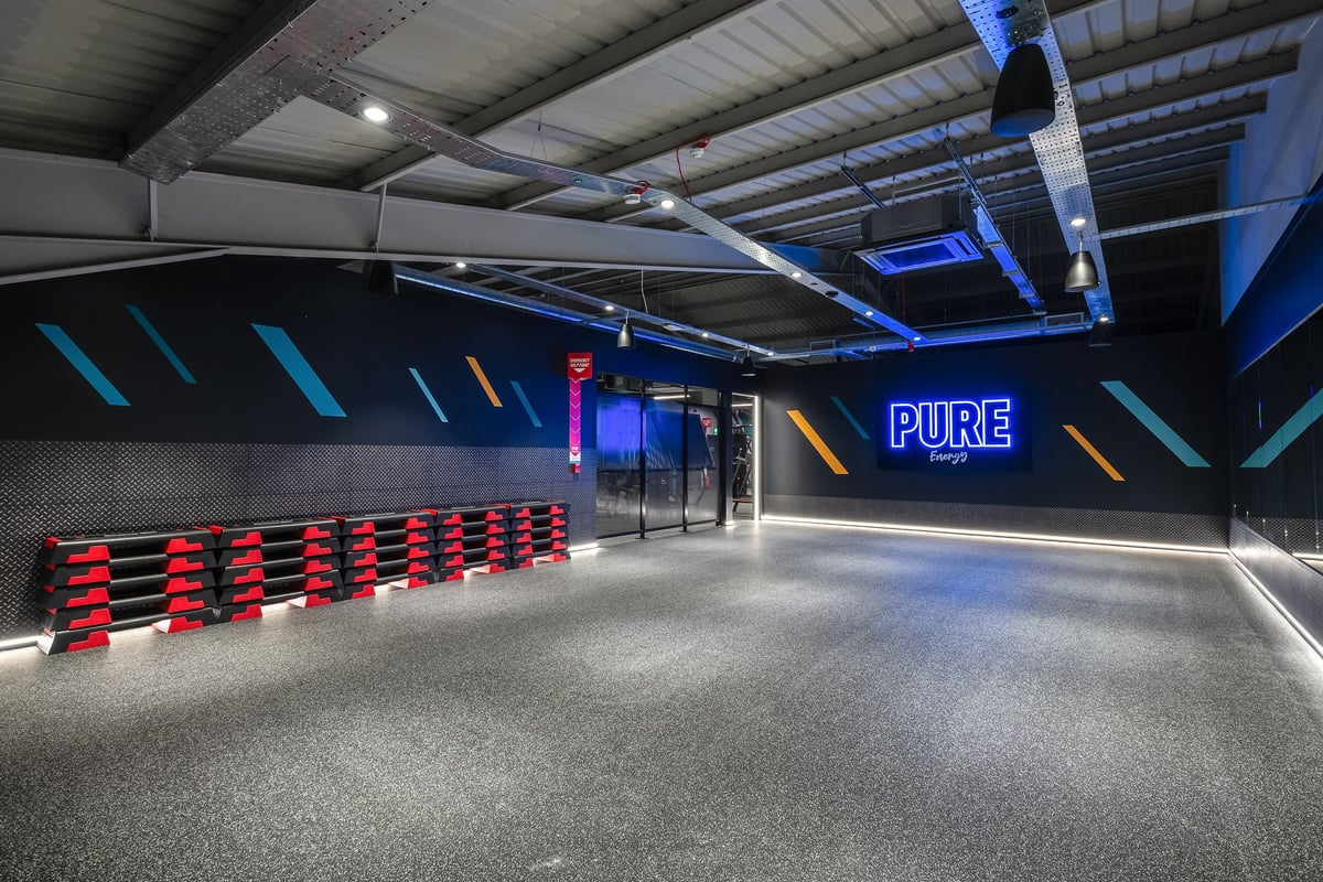PureGym Llantrisant: Red benches, neon lighting, mirrored walls, and rubberized flooring in a modern gym studio interior.