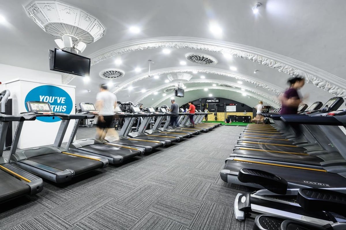 PureGym London Wandsworth: Rows of treadmills and illuminated ceiling arches in a modern gym setting.