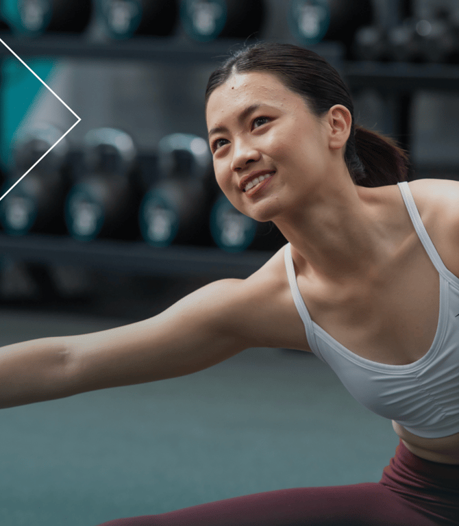 A smiling female PureGym member stretching in a gym
