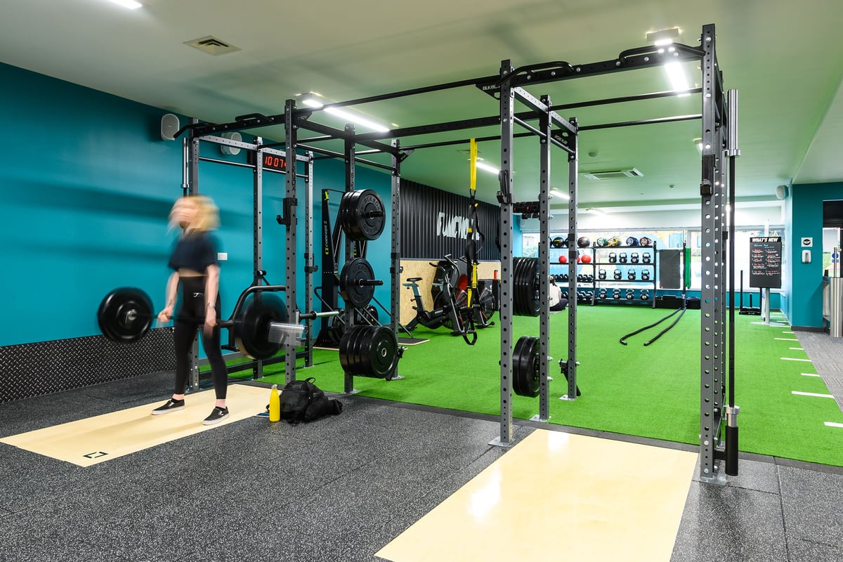 PureGym Didcot: Squat racks, bumper plates, turf area, rubberized flooring in a gym with teal and green walls.