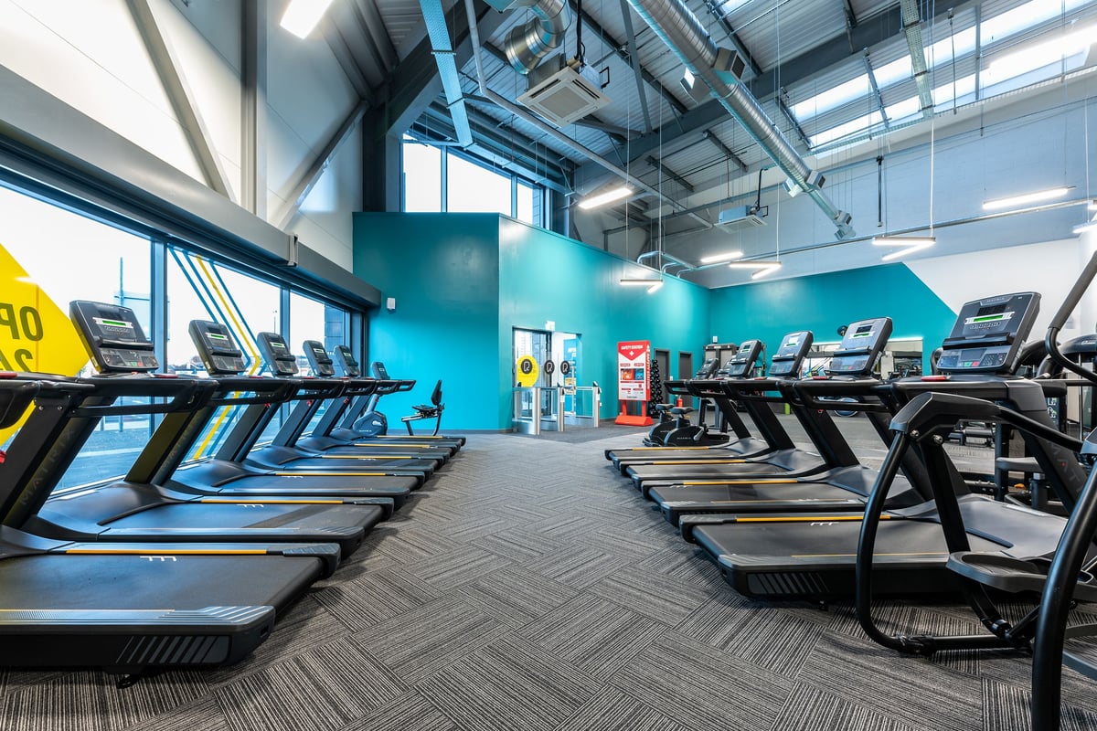 PureGym Kirkby: Rows of treadmills and exercise machines in a bright blue-walled gym interior.
