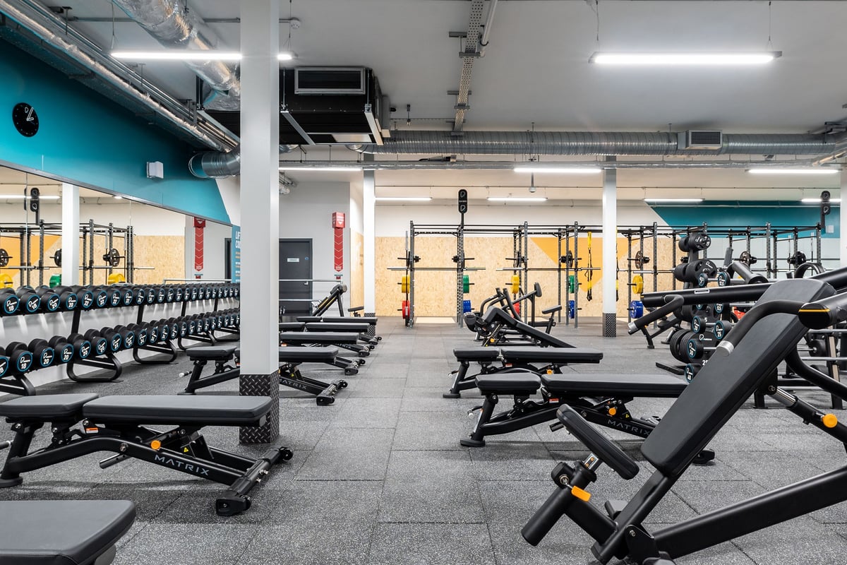PureGym Kettering: Rows of benches, weight racks, free weights, and rubberized flooring in a gym.