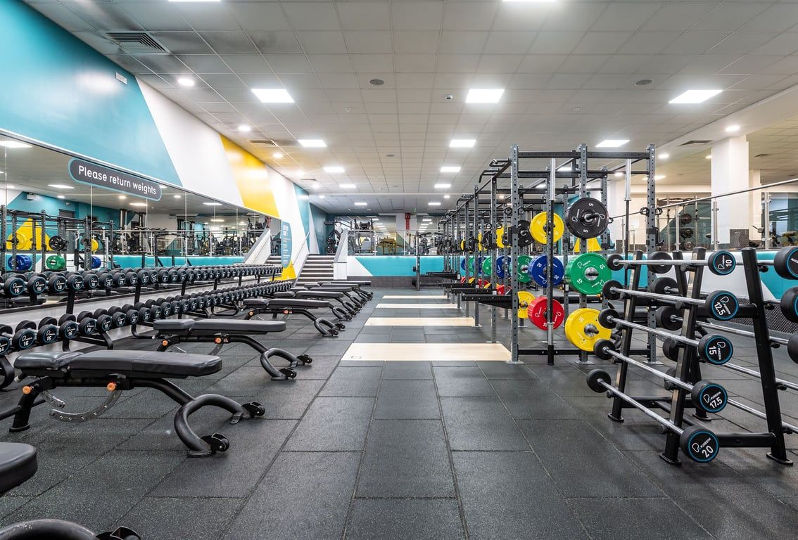 PureGym Harlow: Rows of resistance machines, free weights, benches, and mirrored walls in a bright, colorful gym.