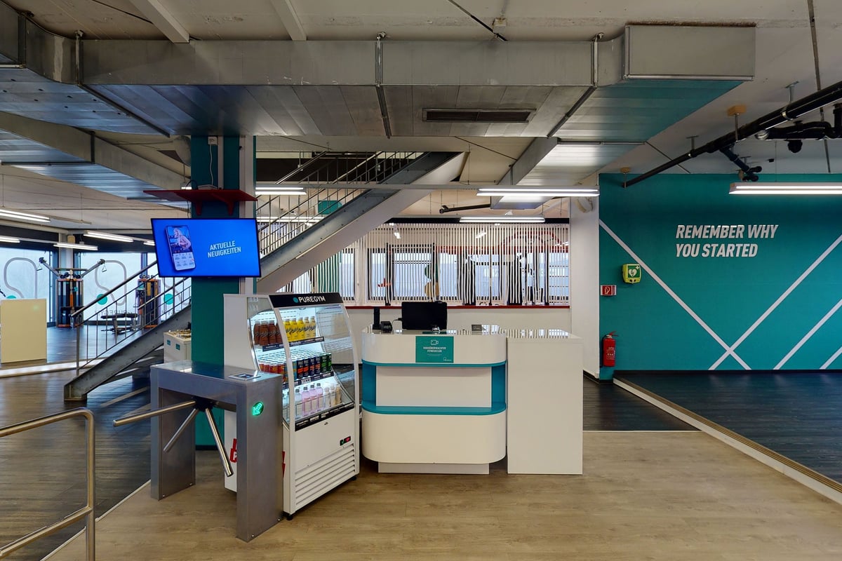 PureGym Uster: Zone de réception avec bornes d'enregistrement, affichage numérique et sièges.