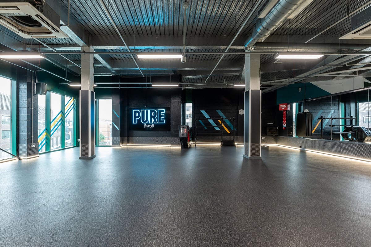 PureGym Newcastle Eldon Garden: Open gym area with exposed ceilings, pillars, and a neon "PURE" sign on the wall.