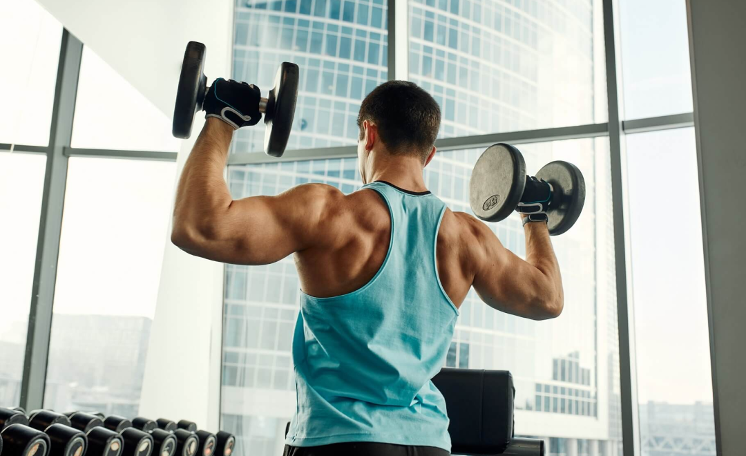 Mann führt Hantel-Schulterpresse in hochgelegenem Fitnessstudio mit Stadtaussicht durch.