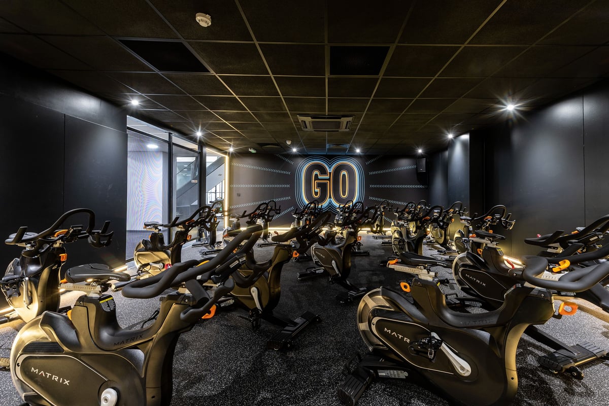 PureGym London Bayswater: Rows of stationary bikes in a dimly lit studio with 'GO' illuminated sign.