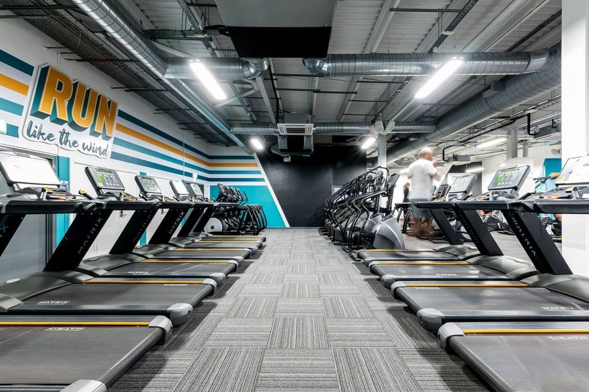 PureGym Cambridge Leisure Park: Rows of treadmills in a well-lit gym with motivational signage along the walls.