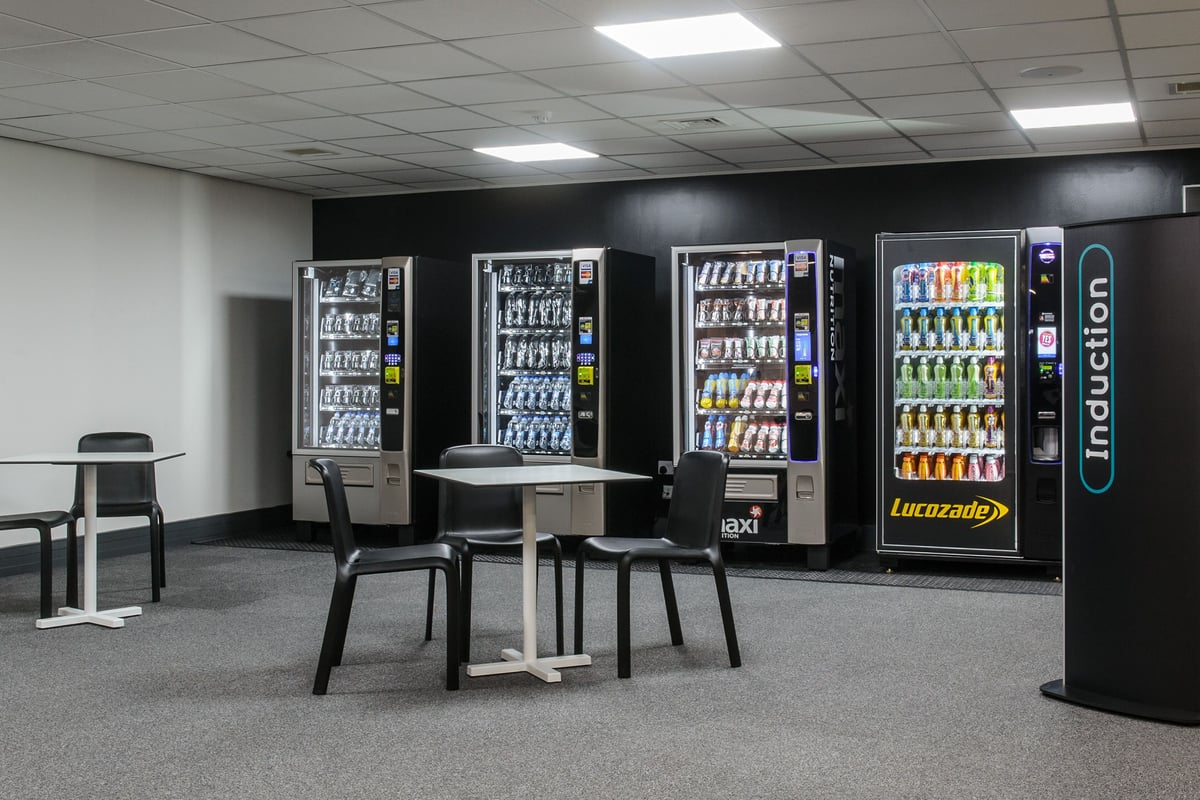 PureGym Bedford Heights: Food and beverage vending machines, tables and chairs, and an Induction sign.