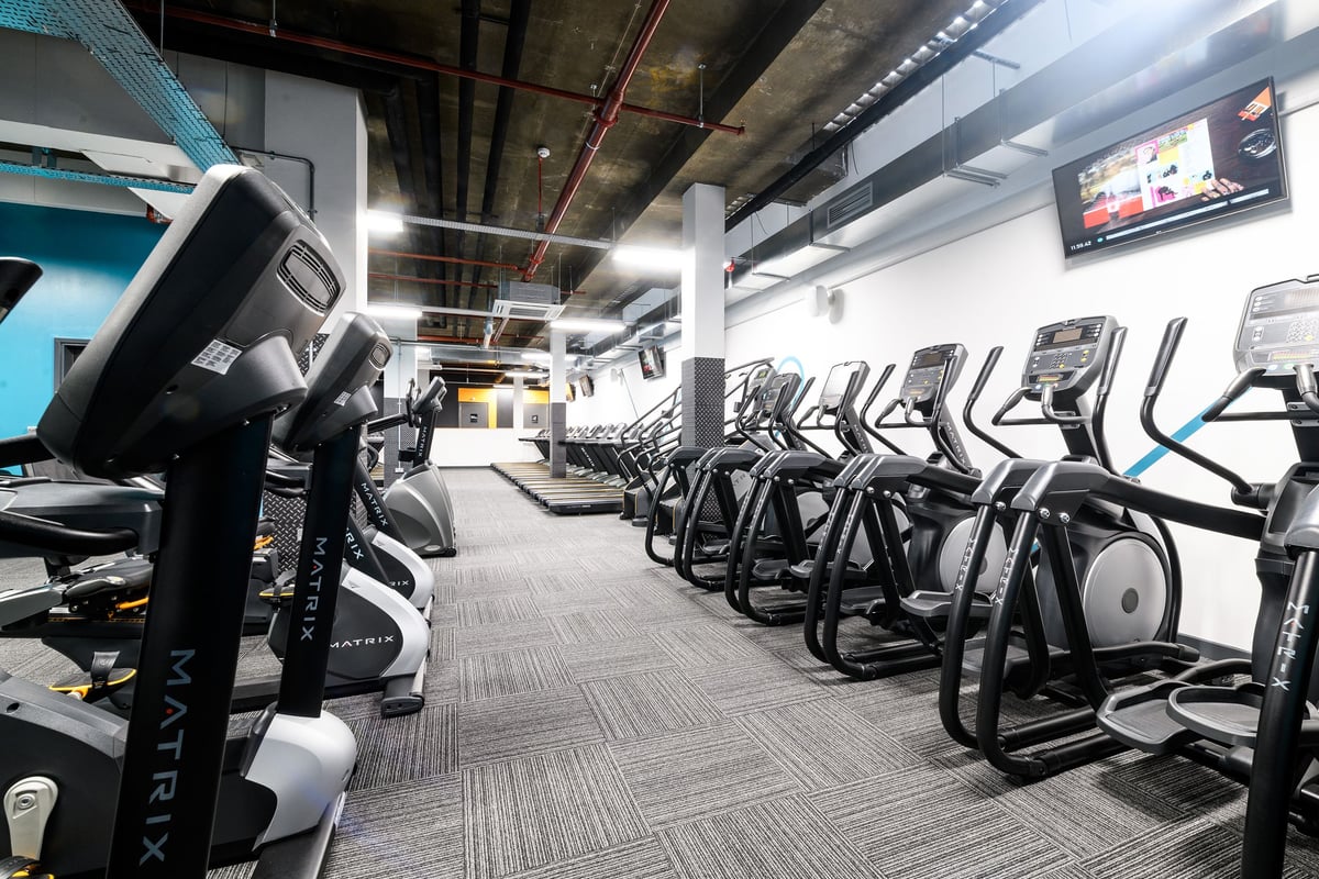PureGym London Tottenham Court Road: Rows of modern cardio equipment in a dimly lit gym with exposed ceiling and TV monitors.