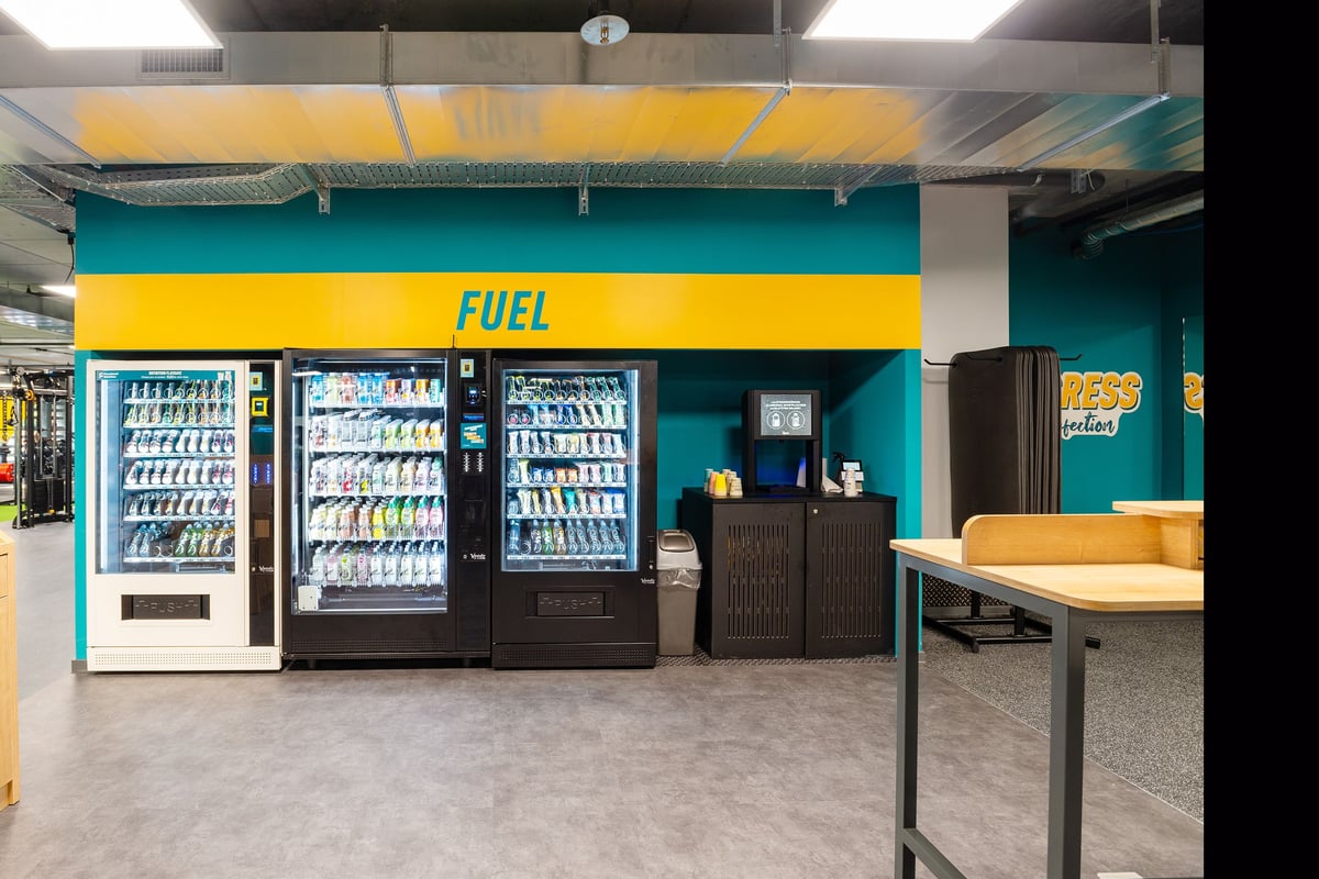 PureGym Genf Le Bouchet: Refrigerators with chilled beverages and snacks, table with chairs, labelled as "FUEL" area.