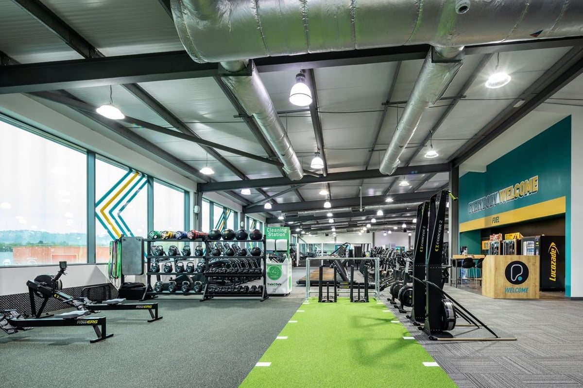 PureGym Cardiff Gate: Weight racks, free weights, turf area, mirrored walls in a modern gym studio with suspended lighting.