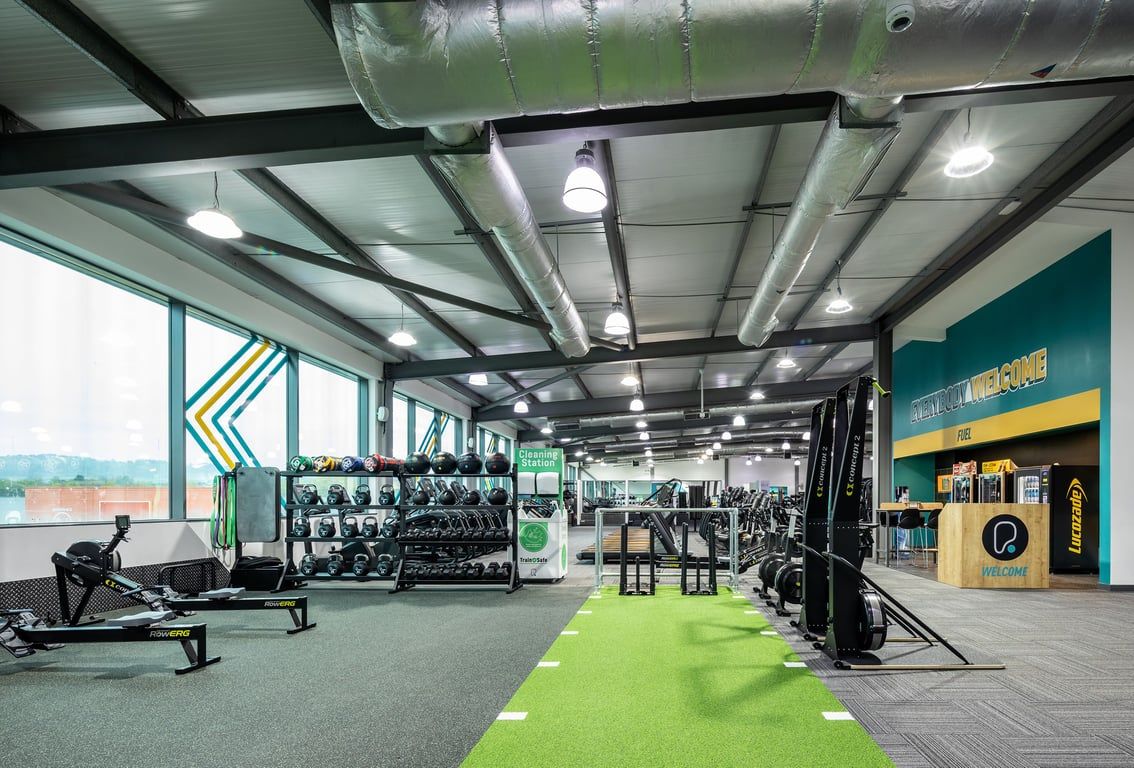 PureGym Cardiff Gate: Weight racks, free weights, turf area, mirrored walls in a modern gym studio with suspended lighting.