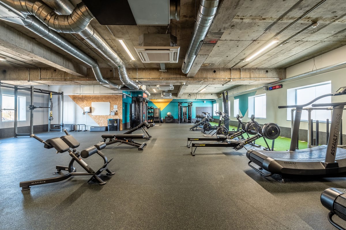 PureGym London Swiss Cottage: Gym interior with weight benches, treadmills, exercise bikes, and ventilation ducts on ceiling.