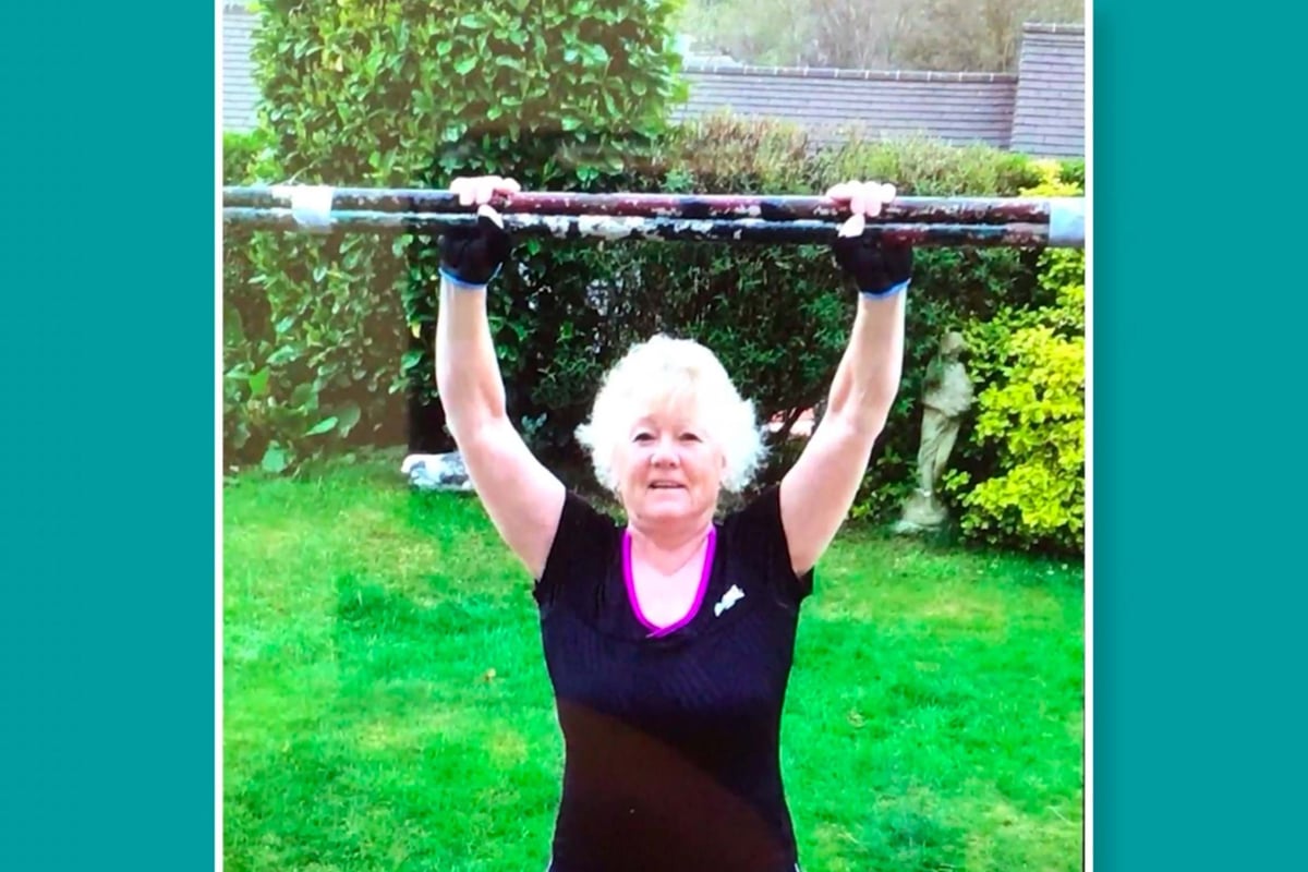 Woman in black top holding a rusty metal bar above her head in a garden