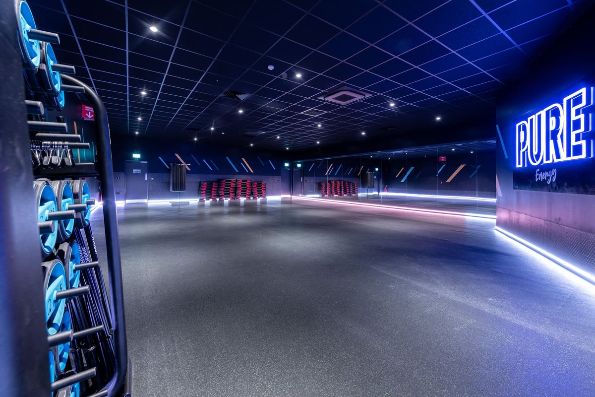 PureGym Aintree: Futuristic gym interior with neon lighting, treadmills, and weight equipment.