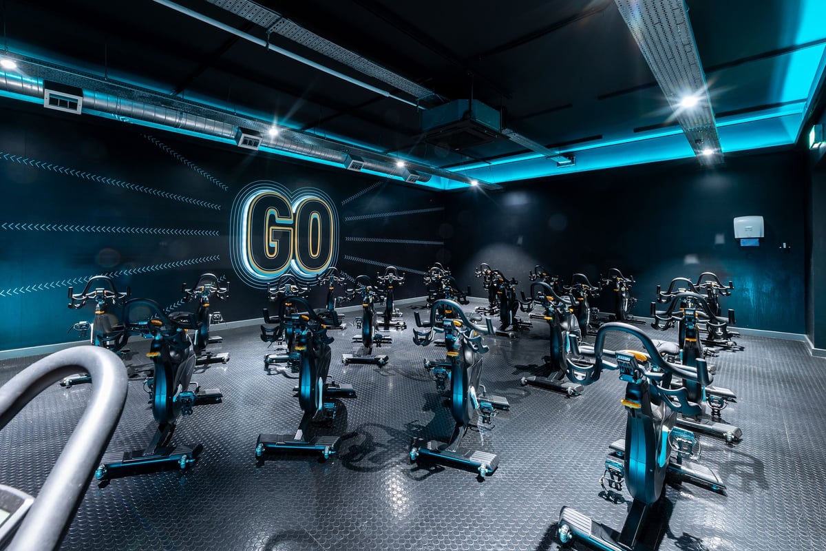 PureGym Stevenage: Rows of stationary bikes in a dimly lit studio with neon "GO" signage.