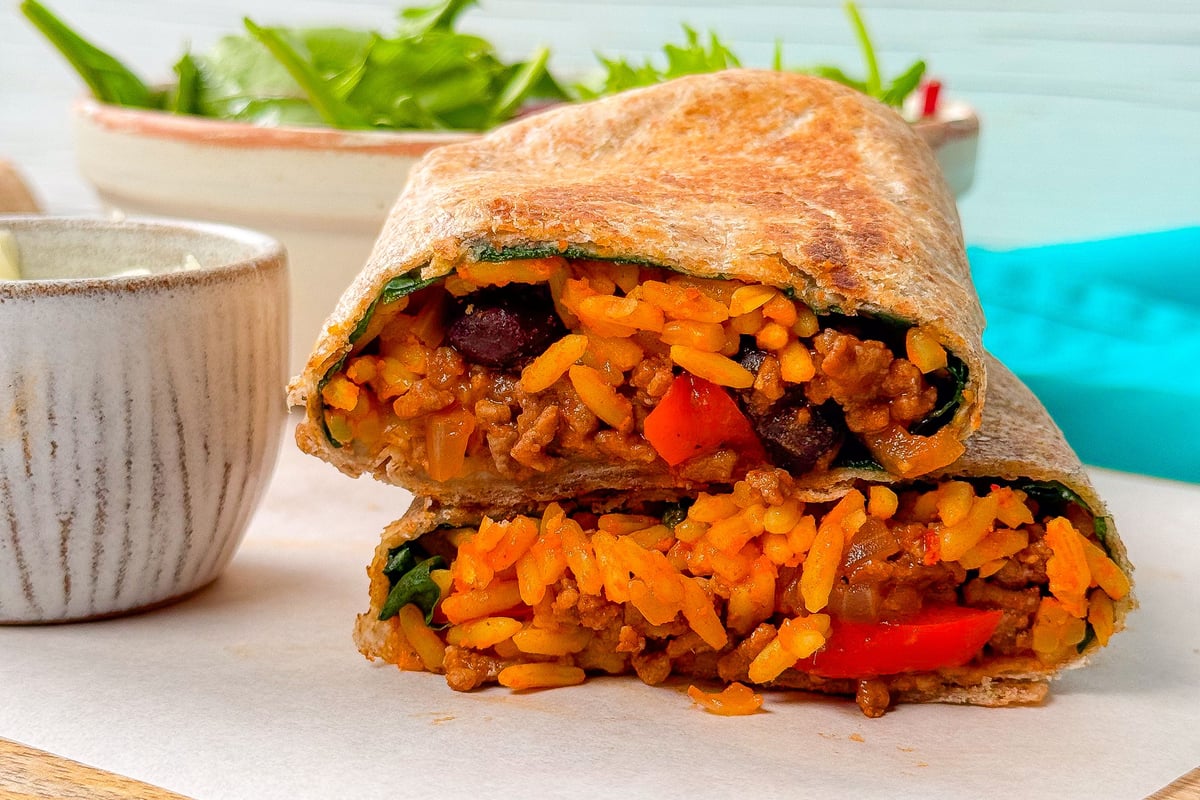 Wrap cut in half showing rice, beans, minced meat, and vegetables inside on wooden board