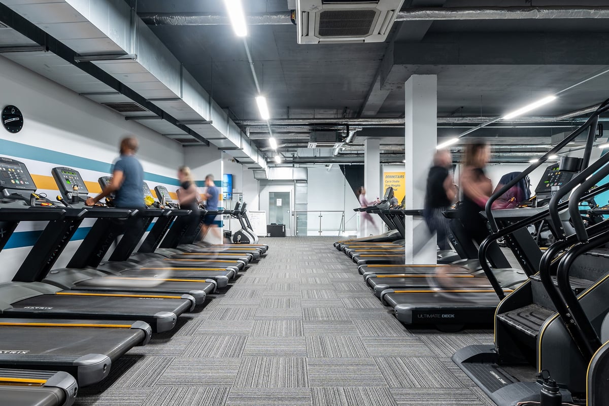 PureGym London Hammersmith Palais: Rows of treadmills and elliptical machines in a dimly lit gym interior.
