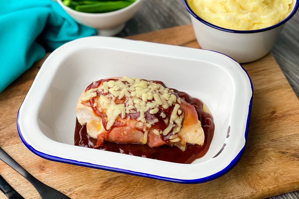 Chicken breast topped with bacon, barbecue sauce and melted cheese in white dish
