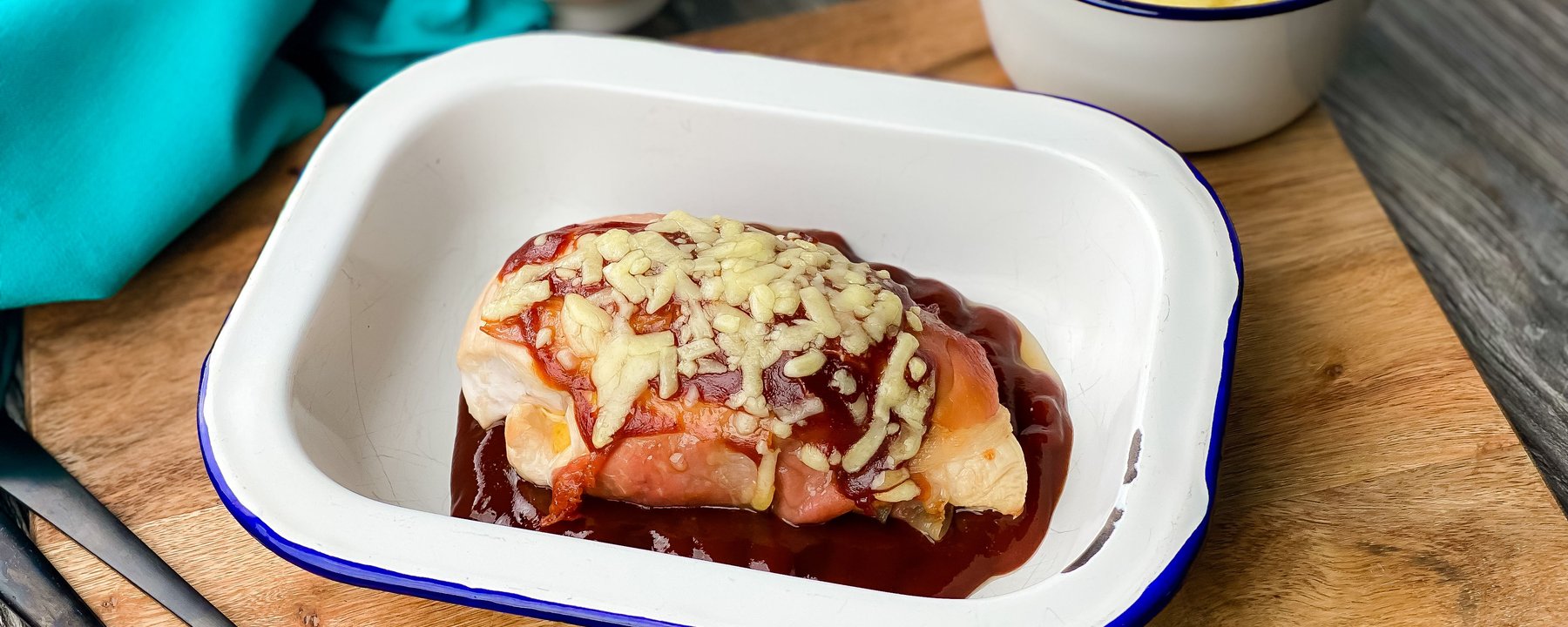 Chicken breast topped with bacon, barbecue sauce and melted cheese in white dish
