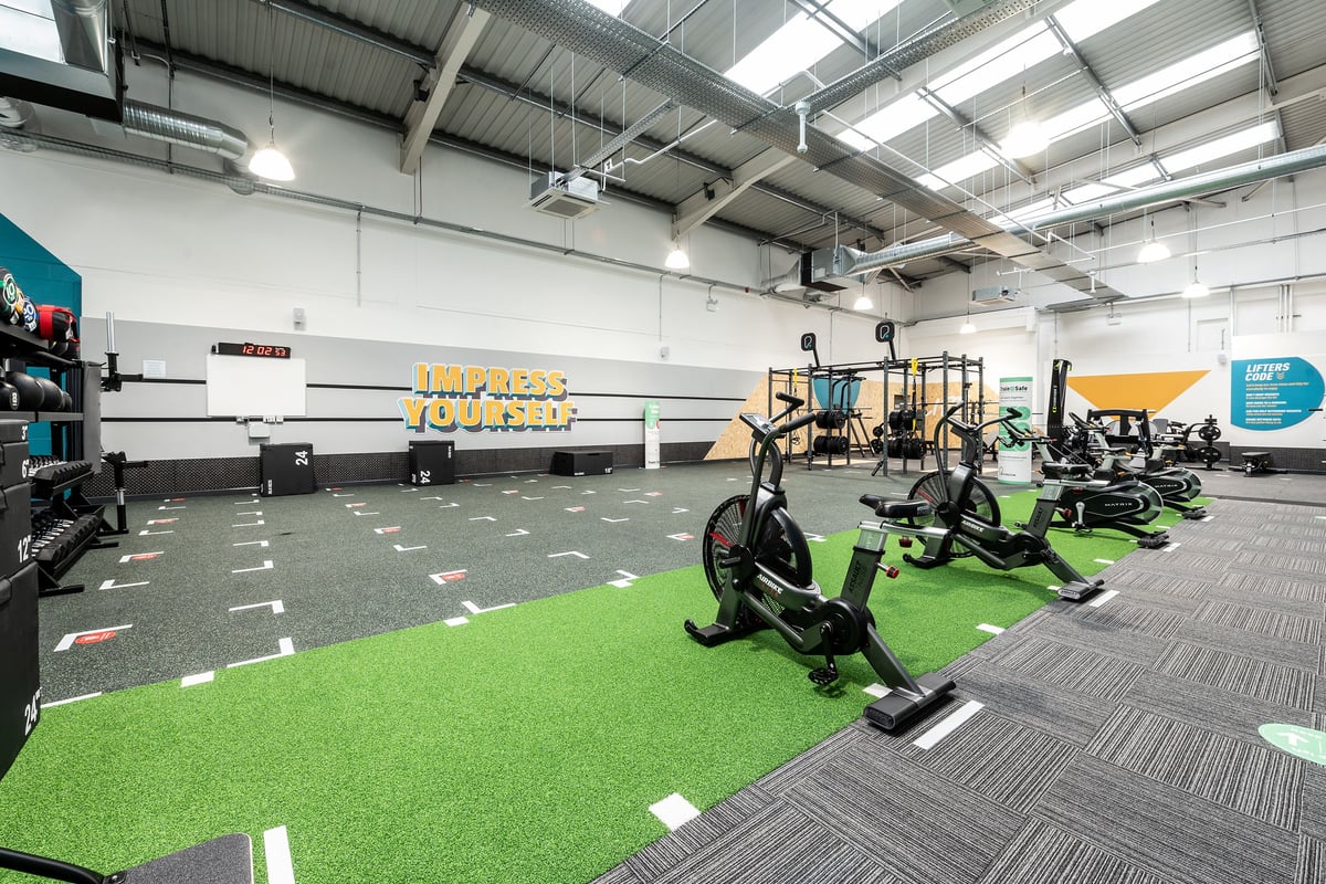 PureGym Stockport North: Fitness studio with turf area, exercise machines, free weights, and mirrors on wall.
