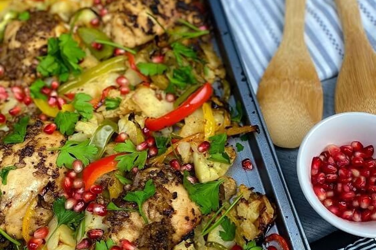 Roasted chicken with mixed peppers, cauliflower, parsley, and pomegranate seeds on tray.
