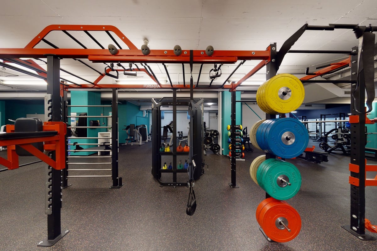 PureGym Basel Dreispitz: Gym space with rig frames, weight plates, resistance bands, and rubberized flooring.