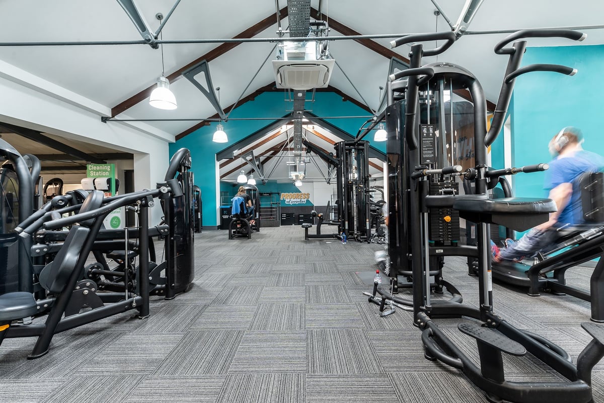 PureGym London Bayswater: Gym interior with exercise machines, weight racks, rubberized flooring, and teal accented walls.