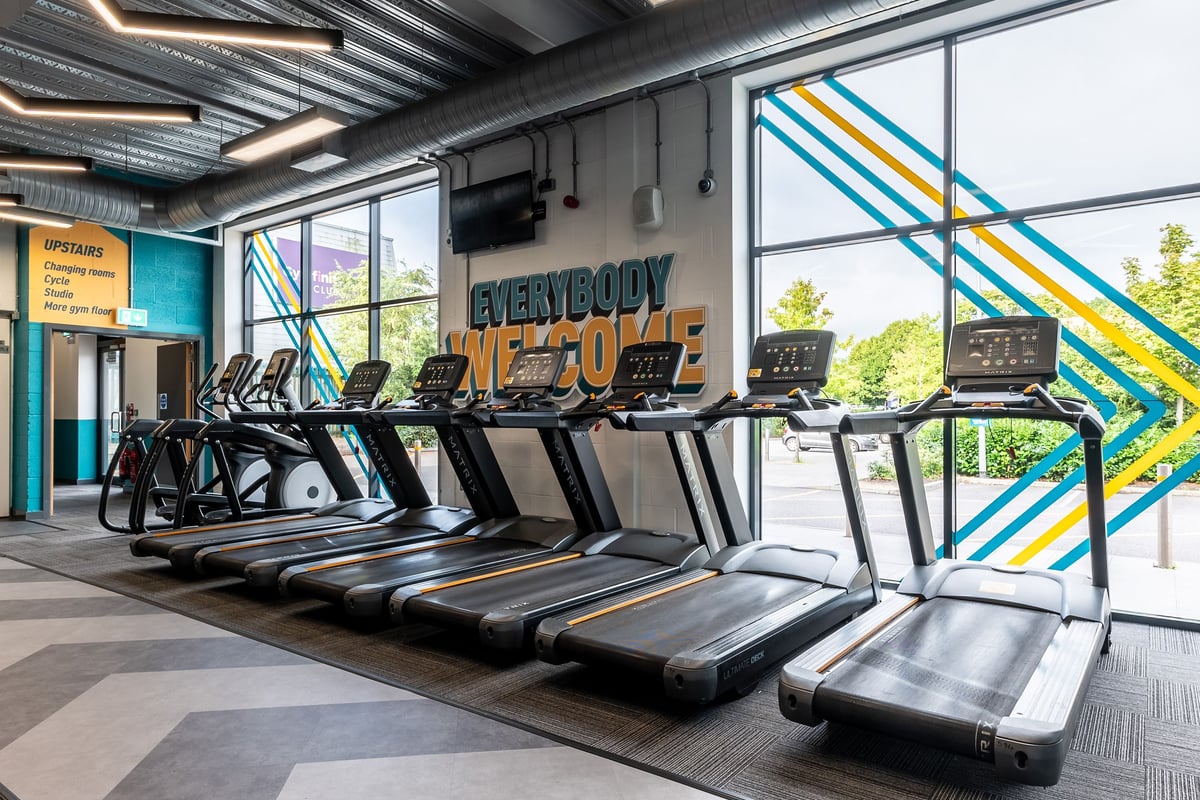 PureGym Reading Basingstoke Road: Rows of treadmills, vibrant geometric wall art, and signage saying "Everybody Fit Out".