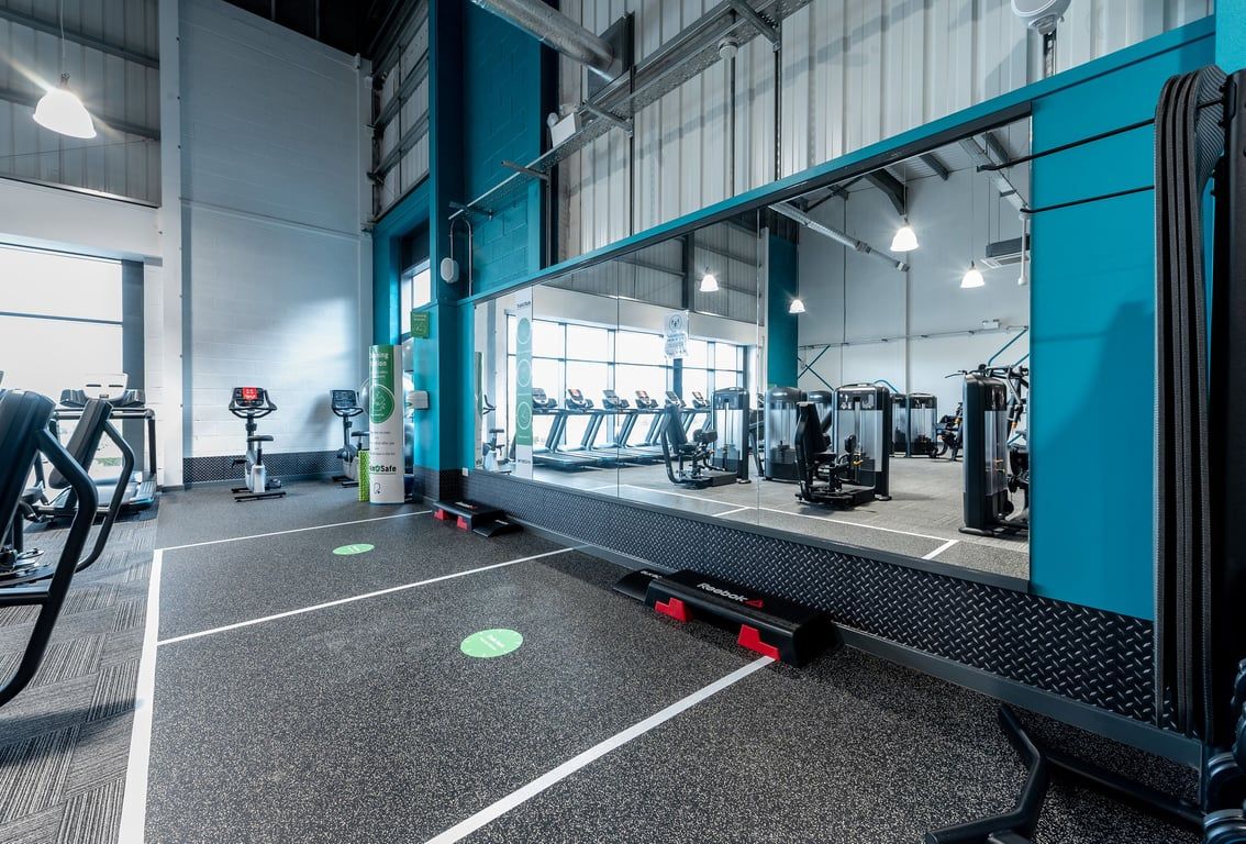 PureGym Birmingham Longbridge: Strength racks, rubberized turf, weightlifting platforms, and mirrors lining the gym interior.
