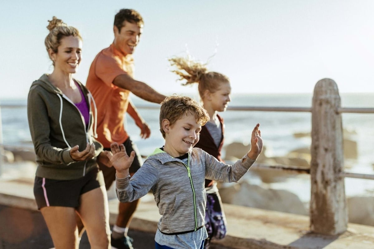 Family of four walking and smiling along a seaside promenade in sportswear
