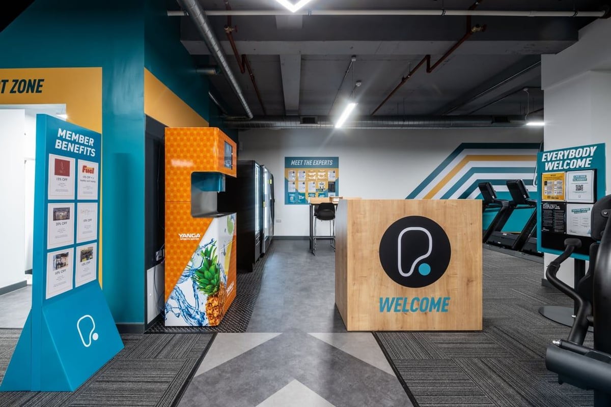 PureGym London Kingston: Welcome zone with podium, signage, and food and beverage vending machines.