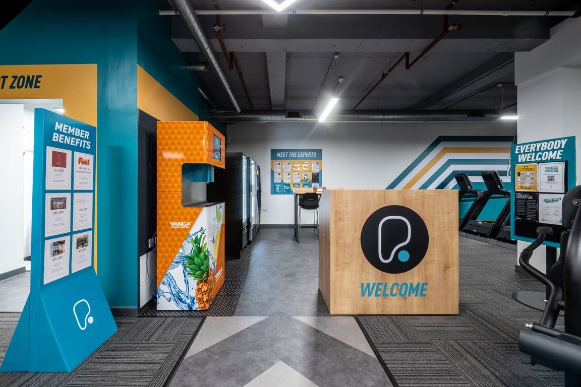 PureGym London Kingston: Welcome zone with podium, signage, and food and beverage vending machines.