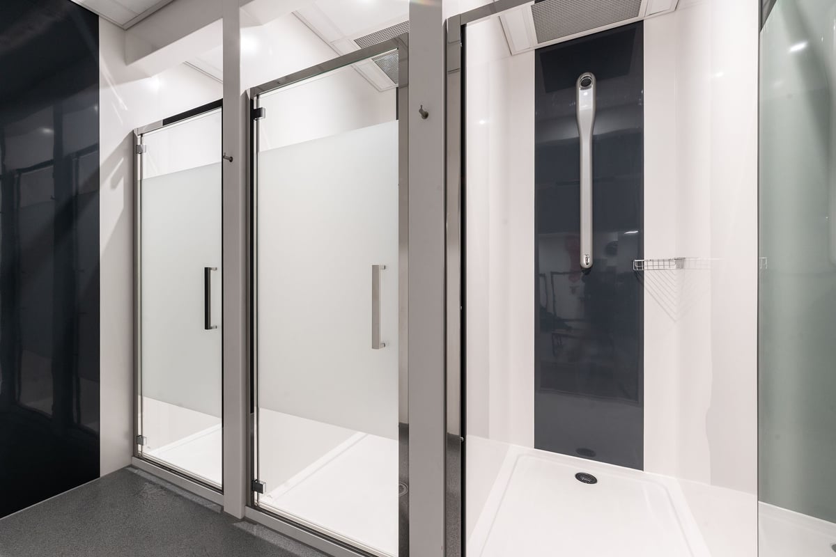 PureGym London Wood Green: Shower area with glass stalls, tiled floors, and privacy partitions.
